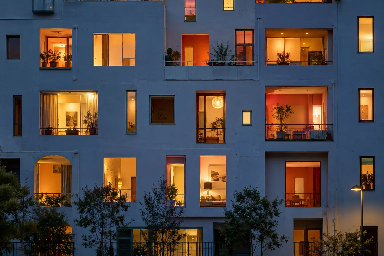 Blue-hour facade with many distinct windows illuminated in warm colors